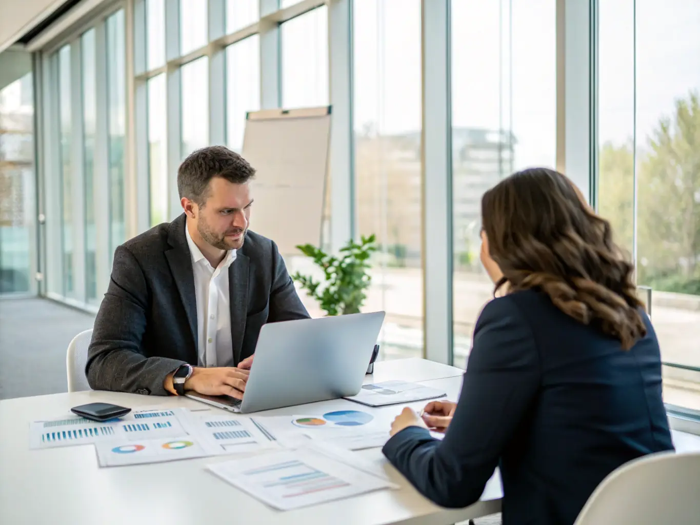A consultant working with a client on a strategic business analysis session, reviewing charts and data on a laptop in a modern office setting.